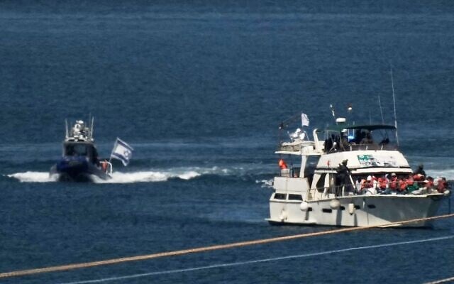 Des militants vêtus de gilets de sauvetage orange sont assis à bord d'un bateau de la flottille Sumud à destination de Gaza, tandis que des soldats de la marine israélienne le conduisent vers le port d'Ashdod, en Israël, le 2 octobre 2025, après l'avoir intercepté alors qu'il s'approchait de la côte de Gaza. (Crédit : AP Photo/Leo Correa)