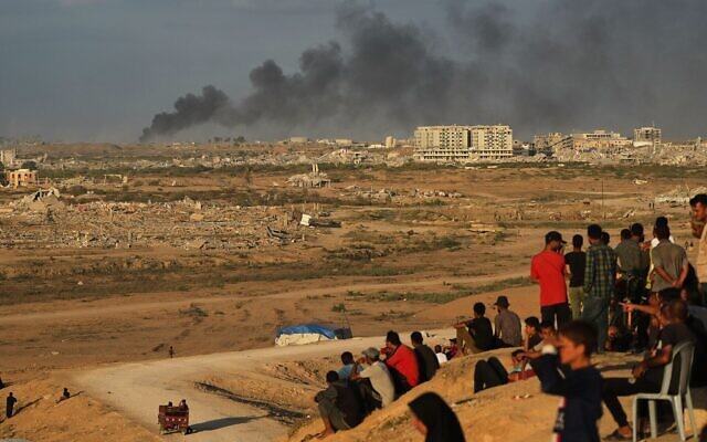 Des Palestiniens déplacés regardent la fumée s'élever après les frappes militaires israéliennes alors qu'ils se rassemblent sur la route côtière près de Wadi Gaza, dans le centre de la bande de Gaza, le 9 octobre 2025. (Crédit : AP Photo/Abdel Kareem Hana)