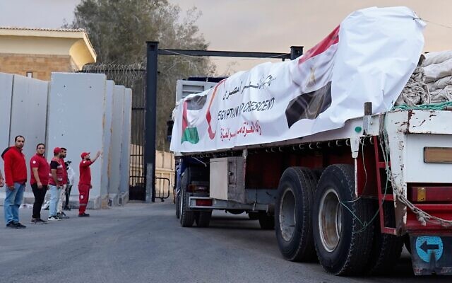 Des membres du Croissant-Rouge égyptien surveillent les camions transportant de l'aide humanitaire alors qu'ils entrent au poste-frontière de Rafah entre l'Égypte et la bande de Gaza, suite à un accord entre Israël et le Hamas sur un cessez-le-feu, le 12 octobre 2025. (Crédit : AP/Mohamed Arafat)
