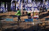 Un employé nettoie la place des otages, derrière les images des otages assassinés Bipin Joshi et Yossi Sharabi, à Tel Aviv, en Israël, le mardi 14 octobre 2025. (Crédit : AP Photo/Francisco Seco)