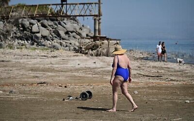 Des personnes marchent sur le rivage de la mer de Galilée, là où il y avait auparavant de l'eau, en passant devant des infrastructures autrefois submergées, dans le kibboutz Ginosar, dans le nord d'Israël, le 4 octobre 2025. (Crédit : Michael Giladi/Flash90)