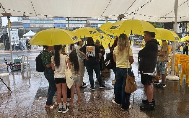 Des personnes s'abritant de la pluie, sur la Place des Otages, à Tel Aviv, le 9 octobre 2025. (Crédit : Ben Sales/Times of Israel)