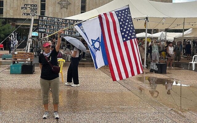 Miki Ziv agitant le drapeau américain et le drapeau d'Israël, sur la Place des Otages, à Tel Aviv, le 9 octobre 2025. (Crédit : Ben Sales/Times of Israel)