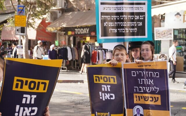 Des enfants ultra-orthodoxes posent avec des pancartes sur lesquelles on peut lire « La Russie est là ! » lors d'une manifestation contre la conscription des hommes haredim dans l'armée israélienne, à Jérusalem, le 30 octobre 2025. (Crédit : Charlie Summers/Times of Israel)