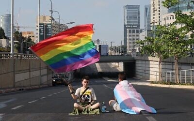 Des manifestants brandissent des drapeaux arc-en-ciel et transgenres, assis sur une route, lors d'une manifestation contre les projets de réforme judiciaire du gouvernement, à Tel Aviv, le 18 juillet 2023. (Crédit : JACK GUEZ/AFP)