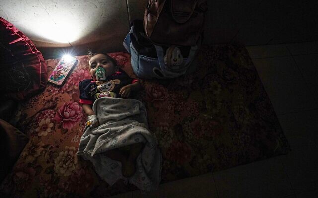 Illustration : Un bébé allongé sur un matelas posé à même le sol éclairé par la lampe torche d'un téléphone, après une coupure partielle d'électricité, à l'hôpital al-Aqsa Martyrs, à Deir al-Balah, le 23 mai 2024. (Crédit : Bashar Taleb/AFP)