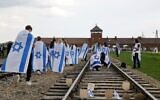 Des participants à la Marche des vivants annuelle organisée en hommage aux victimes de la Shoah arborent le drapeau israélien, alors qu’ils marchent le long de la voie ferrée menant à l’entrée de l’ancien camp d’extermination nazi d’Auschwitz-Birkenau en Pologne, le 24 avril 2025. (Crédit : Wojtek RADWANSKI/AFP)