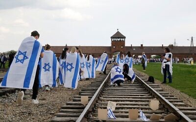 Des participants à la Marche des vivants annuelle organisée en hommage aux victimes de la Shoah arborent le drapeau israélien, alors qu’ils marchent le long de la voie ferrée menant à l’entrée de l’ancien camp d’extermination nazi d’Auschwitz-Birkenau en Pologne, le 24 avril 2025. (Crédit : Wojtek RADWANSKI/AFP)