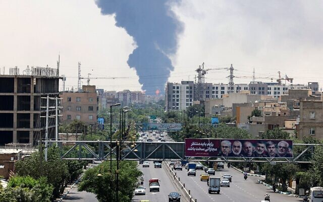 Les portraits des généraux et des scientifiques nucléaires iraniens tués lors de l'attaque israélienne du 13 juin sont affichés au-dessus d'une route, tandis qu'un panache de fumée épaisse et des flammes s'élèvent d'une raffinerie de pétrole dans le sud de Téhéran, après avoir été touchée par une frappe israélienne nocturne, le 15 juin 2025. (Crédit : ATTA KENARE / AFP) Les portraits des généraux et des scientifiques nucléaires iraniens tués lors de l'attaque israélienne du 13 juin sont affichés au-dessus d'une route, tandis qu'un panache de fumée épaisse et des flammes s'élèvent d'une raffinerie de pétrole dans le sud de Téhéran, après avoir été touchée par une frappe israélienne nocturne, le 15 juin 2025. (Crédit : ATTA KENARE / AFP)