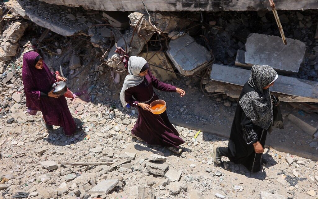 Des Palestiniennes transportent des casseroles contenant de la nourriture collectée dans une cuisine caritative qui fournit des repas chauds dans le quartier de Rimal, à Gaza, le 18 juin 2025. (Crédit : Omar AL-QATTAA / AFP)