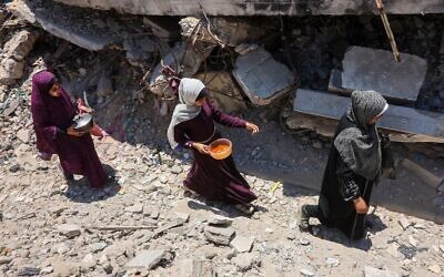 Des Palestiniennes transportent des casseroles contenant de la nourriture collectée dans une cuisine caritative qui fournit des repas chauds dans le quartier de Rimal, à Gaza, le 18 juin 2025. (Crédit : Omar AL-QATTAA / AFP)