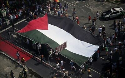 Des militants brandissent un immense drapeau palestinien lors de la "Grande Marche populaire" organisée en marge de la COP30, la conférence des Nations unies sur les changements climatiques, à Belém, dans l'État du Pará, au Brésil, le 15 novembre 2025. (Crédit : Mauro PIMENTEL / AFP)