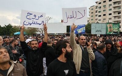 Un homme brandit une pancarte sur laquelle on peut lire en arabe « Libération des détenus » (g) et « Non au meurtre », alors que des personnes participent à une manifestation sur la place al-Azhari, suite aux récentes attaques contre la communauté minoritaire alaouite, une branche de l'islam chiite, dans la ville côtière de Lattaquié, en Syrie, le 25 novembre 2025. (Crédit : HAIDAR MUSTAFA / AFP)