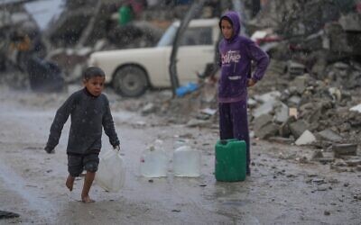 Un garçon pieds nus marche sous la pluie en portant un jerrican en plastique rempli d'eau dans le quartier de Sheikh Radwan à Gaza-City, le 14 novembre 2025. (Crédit : AP Photo/Jehad Alshrafi)