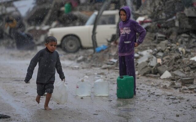 Un garçon pieds nus marche sous la pluie en portant un jerrican en plastique rempli d'eau dans le quartier de Sheikh Radwan à Gaza-City, le 14 novembre 2025. (Crédit : AP Photo/Jehad Alshrafi)
