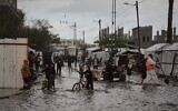 Des Palestiniens marchent dans une rue inondée à côté d'un campement de tentes  après de fortes pluies à Deir al-Balah, dans le centre de la bande de Gaza, mardi 25 novembre 2025. (Crédit : AP Photo/Abdel Kareem Hana)