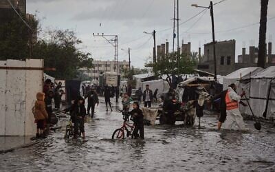 Des Palestiniens marchent dans une rue inondée à côté d'un campement de tentes après de fortes pluies à Deir al-Balah, dans le centre de la bande de Gaza, mardi 25 novembre 2025. (Crédit : AP Photo/Abdel Kareem Hana) Des Palestiniens marchent dans une rue inondée à côté d'un campement de tentes après de fortes pluies à Deir al-Balah, dans le centre de la bande de Gaza, mardi 25 novembre 2025. (Crédit : AP Photo/Abdel Kareem Hana)
