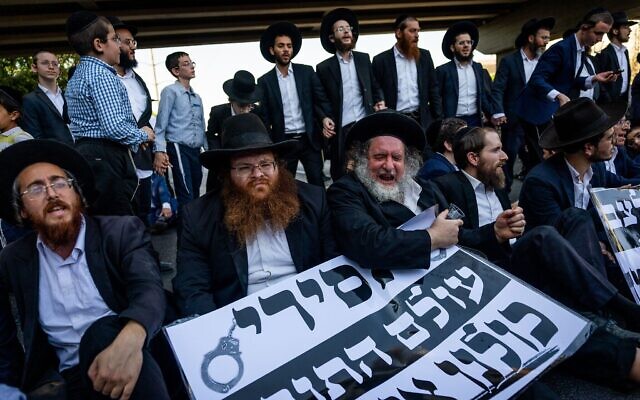 Des manifestants ultra-orthodoxes affrontent la police lors d'un rassemblement contre l'arrestation d'hommes haredim qui ne se sont pas présentés à leur service militaire, sur la Route 4 près de Bnei Brak, le 19 août 2025. Ils brandissent une pancarte sur laquelle on peut lire : "Prisonniers du monde de la Torah : nous sommes avec vous". (Crédit : Yonatan Sindel/Flash90)