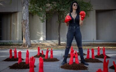 Une femme porte des gants de boxe  au milieu de mains rouges symbolisant les femmes assassinées lors d'un happening organisé à l'occasion de la Journée internationale pour l'élimination des violences faites aux femmes devant la Her Academy, un établissement de formation pour les survivantes de la prostitution et des violences sexuelles, à Tel Aviv, le 24 novembre 2025. (Crédit : Miriam Alster/Flash90)