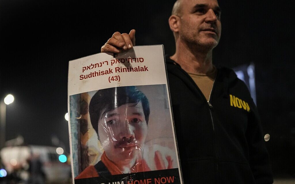 Un homme tenant une photo de Sudthisak Rinthalak lors d'un rassemblement appelant à la libération des deux derniers otages dont les corps sont retenus à Gaza, près de Sderot, le 29 novembre 2025. (Crédit : Tsafrir Abayov/Flash90)