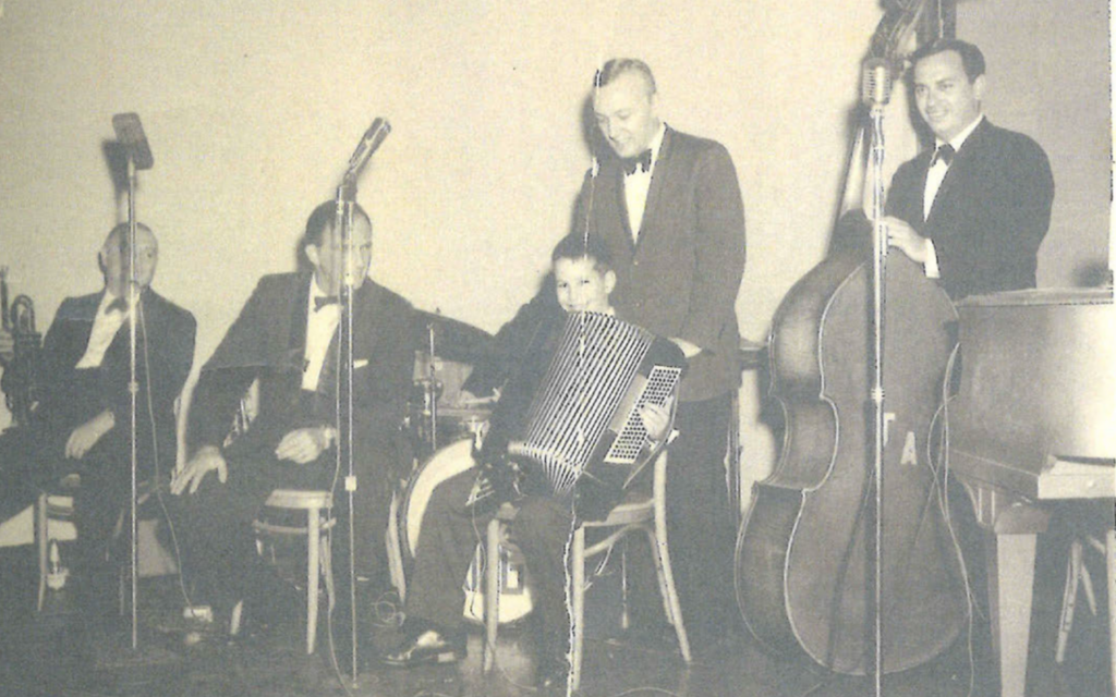 Le jeune Jeffrey Epstein joue de l'accordéon lors d'une bar-mitzvah, accompagné par un groupe de musiciens. Une note manuscrite en bas de la photo, invisible ici, indique "Aaron Brown Bar Mitzvah, Wynn Hotel, Philly, Sept. 23, 1961". (Crédit : Extrait du livre d'anniversaire d'Epstein via JTA) Le jeune Jeffrey Epstein joue de l'accordéon lors d'une bar-mitzvah, accompagné par un groupe de musiciens. Une note manuscrite en bas de la photo, invisible ici, indique "Aaron Brown Bar Mitzvah, Wynn Hotel, Philly, Sept. 23, 1961". (Crédit : Extrait du livre d'anniversaire d'Epstein via JTA)