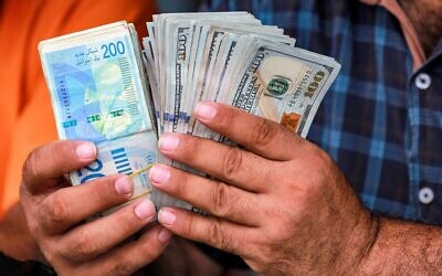 Photo d'Illustration : un homme compte des liasses de billets en shekels israéliens et en dollars américains dans un bureau de change informel à Deir al-Balah, dans le centre de la bande de Gaza, le 2 juillet 2024. (Crédit : Bashar TALEB / AFP)