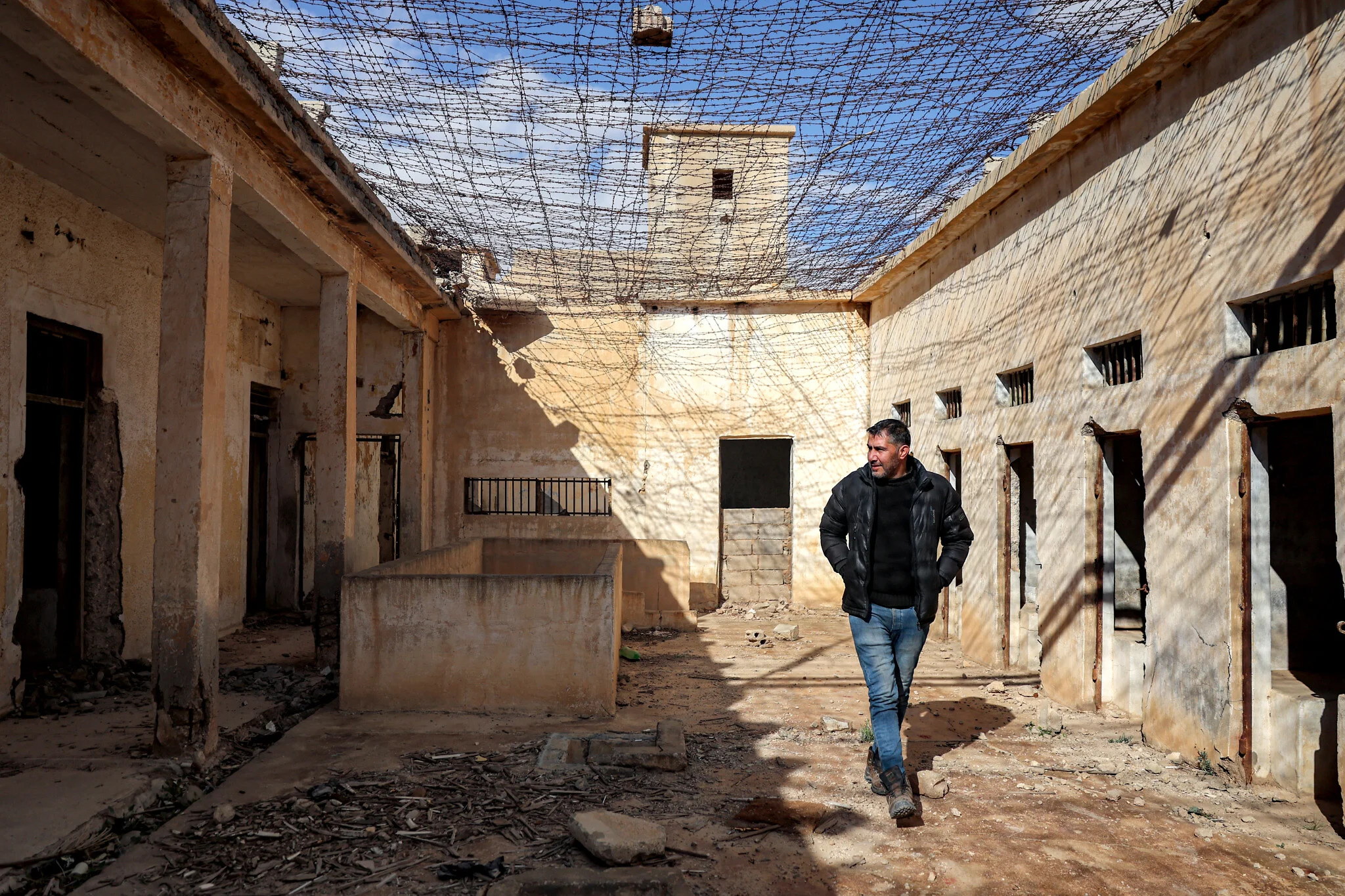 Un habitant passe devant des cellules alors qu’il guide des journalistes visitant le complexe pénitentiaire de Palmyre, anciennement utilisé par le gouvernement Assad renversé, dans la ville du centre syrienne de Palmyre, le 7 février 2025. (Crédit : OMAR HAJ KADOUR/AFP) Un habitant passe devant des cellules alors qu’il guide des journalistes visitant le complexe pénitentiaire de Palmyre, anciennement utilisé par le gouvernement Assad renversé, dans la ville du centre syrienne de Palmyre, le 7 février 2025. (Crédit : OMAR HAJ KADOUR/AFP)
