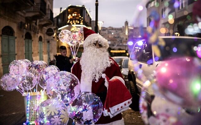 Un homme déguisé en Père Noël vendant des ballons lors d'une cérémonie d'illumination du sapin de Noël, près de la place de la Nativité, à Bethléem, en Cisjordanie, le 6 décembre 2025. (Crédit : John Wessels/AFP) Un homme déguisé en Père Noël vendant des ballons lors d'une cérémonie d'illumination du sapin de Noël, près de la place de la Nativité, à Bethléem, en Cisjordanie, le 6 décembre 2025. (Crédit : John Wessels/AFP)