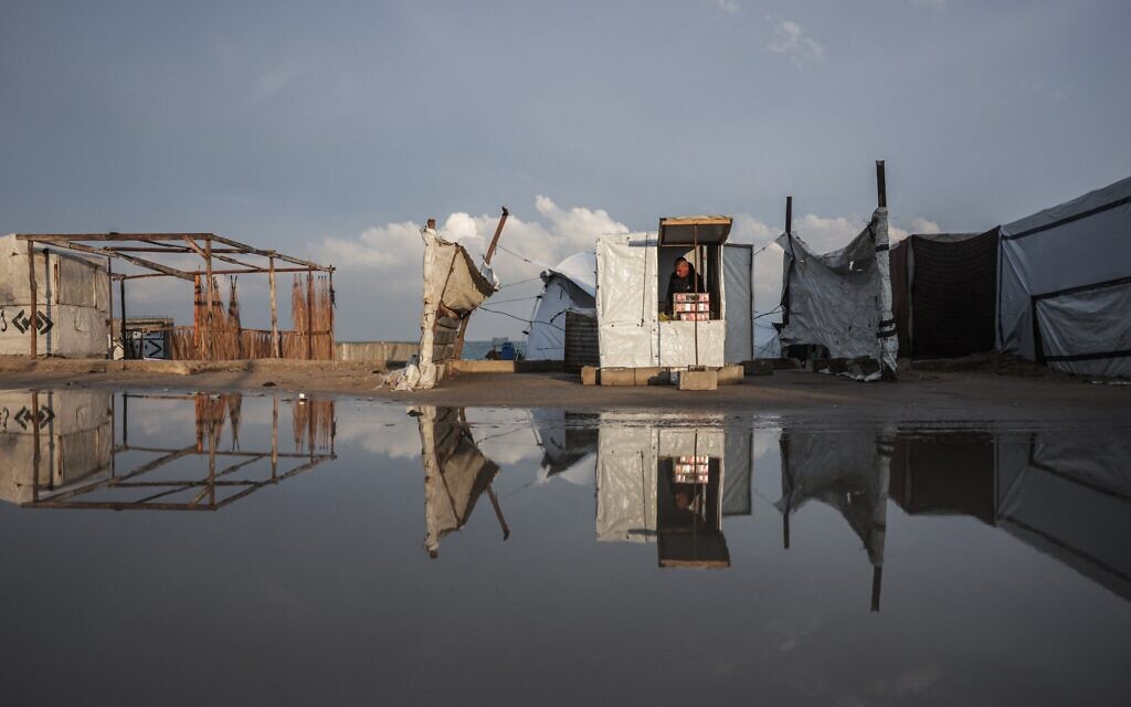 Un Gazaoui installant son étalage de fortune le long d'une route inondée à Deir al-Balah, dans le centre de la bande de Gaza, le 10 décembre 2025 (Crédit : Bashar Taleb/AFP)