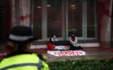 Des manifestants pro-palestiniens sont assis sur le sol avec une pancarte sur laquelle on peut lire "Elbit corrompt la justice", en référence au groupe de défense israélien Elbit, après avoir aspergé de peinture rouge l'extérieur du bâtiment du ministère de la Justice dans le centre de Londres, le 12 décembre 2025. (Crédit : HENRY NICHOLLS / AFP)