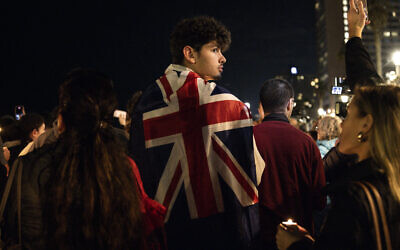 Un homme porte le drapeau britannique sur les épaules lors d'une veillée aux chandelles quelques heures après que deux hommes armés ont abattu des personnes rassemblées sur la plage australienne de Bondi pour la fête juive de Hanoukka, à Tel Aviv, le 14 décembre 2025. (Crédit : JOHN WESSELS / AFP)