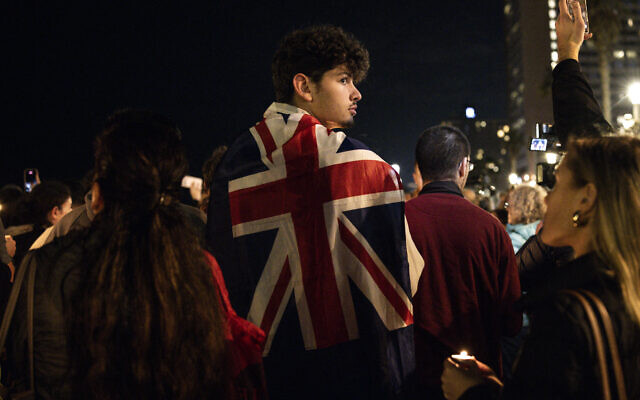 Un homme porte le drapeau britannique sur les épaules lors d'une veillée aux chandelles quelques heures après que deux hommes armés ont abattu des personnes rassemblées sur la plage australienne de Bondi pour la fête juive de Hanoukka, à Tel Aviv, le 14 décembre 2025. (Crédit : JOHN WESSELS / AFP)