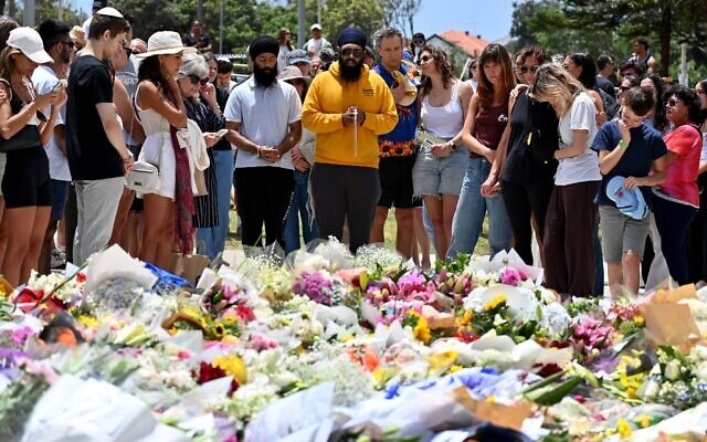 Des personnes en deuil rassemblées autour d'hommages floraux au Bondi Pavilion en mémoire des victimes de la fusillade terroriste meurtrière qui a visé un événement de Hanoukka à Bondi Beach, à Sydney, le 15 décembre 2025. (Crédit : Saeed Khan/AFP)