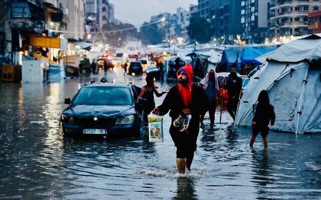 Des Palestiniens marchent dans des rues inondées après de fortes pluies à Gaza-City, le 15 décembre 2025 (Crédit : Omar AL-QATTAA / AFP)
