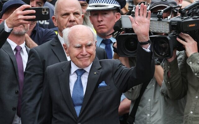 John Howard (au centre) , ancien Premier ministre australien, saluant la foule après avoir déposé des fleurs, en hommage aux victimes de l'attentat terroriste perpétré le premier soir de Hanoukka, devant le Bondi Pavilion, à Sydney, le 16 décembre 2025. (Crédit : David Gray/AFP)