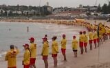 Des sauveteurs australiens observant une minute de silence en hommage aux victimes de la fusillade du 14 décembre,  le long de Bondi Beach, à Sydney, le 20 décembre 2025. (Crédit : Australian Broadcasting Corporation (ABC)/AFP)