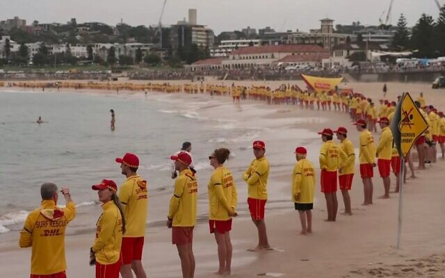 Des sauveteurs australiens observant une minute de silence en hommage aux victimes de la fusillade du 14 décembre,  le long de Bondi Beach, à Sydney, le 20 décembre 2025. (Crédit : Australian Broadcasting Corporation (ABC)/AFP)