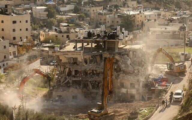 Des pelleteuses démolissent un bâtiment construit sans permis dans la zone de Wadi Qaddum, près du quartier de Silwan à Jérusalem Est, le 22 décembre 2025. (Crédit : AHMAD GHARABLI / AFP)