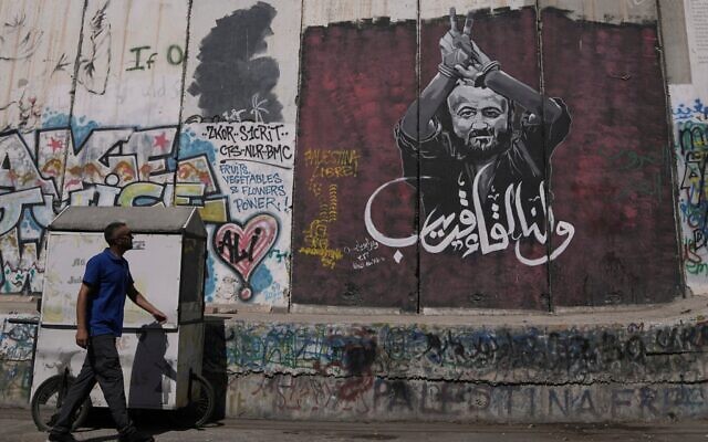 Un homme passant devant une fresque murale représentant le terroriste palestinien condamné à la perpétuité, Marwan Barghouti, avec un message en arabe qui dit « À bientôt », sur la barrière de sécurité israélienne, à Bethléem, en Cisjordanie, le 20 août 2025. (Crédit : Mahmoud Illean/AP)