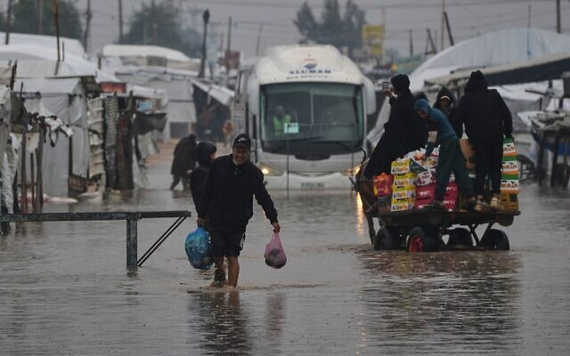 Des Palestiniens marchent dans une rue inondée après de fortes pluies à Khan Younès, dans le sud de la bande de Gaza, le jeudi 11 décembre 2025. (Crédit : AP Photo/Abdel Kareem Hana)