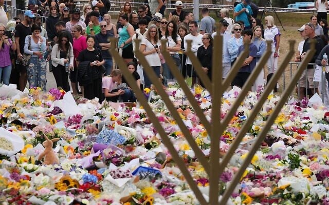 Une hanoukkia près d'un hommage floral tandis que les gens viennent rendre hommage aux victimes de la fusillade meurtrière terroriste qui a visé un événement de Hanoukka le 14 décembre 2025, près du Bondi Pavilion, à Bondi Beach, le 16 décembre 2025. (Crédit : Mark Baker/AP)