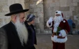 Illustration : Issa Kassissieh, 47 ans, qui accomplit sa 18ᵉ année déguisé en Père Noël, saluant la foule lors de sa tournée annuelle, dans la Vieille Ville de Jérusalem, le 18 décembre 2025. (Crédit : Leo Correa/AP)
