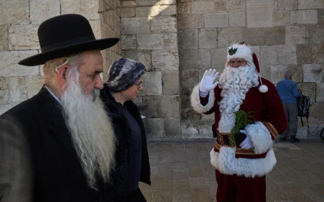 Illustration : Issa Kassissieh, 47 ans, qui accomplit sa 18ᵉ année déguisé en Père Noël, saluant la foule lors de sa tournée annuelle, dans la Vieille Ville de Jérusalem, le 18 décembre 2025. (Crédit : Leo Correa/AP)