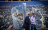 Des passants devant une affiche représentant une tour en spirale en construction à Tel Aviv, le 17 novembre 2025. Illustration (Crédit : Miriam Alster/FLASH90)