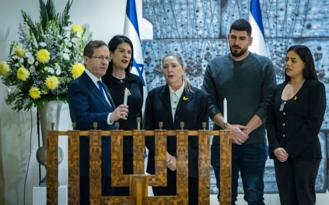 Le président israélien Isaac Herzog et son épouse Michal, accompagnés des membres de la famille du sergent-chef Ran Gvili, dont le corps est détenu par le Hamas à Gaza, allument la première bougie de Hanoukka à la résidence présidentielle à Jérusalem, le 14 décembre 2025. (Crédit : Chaim Goldberg/Flash90)