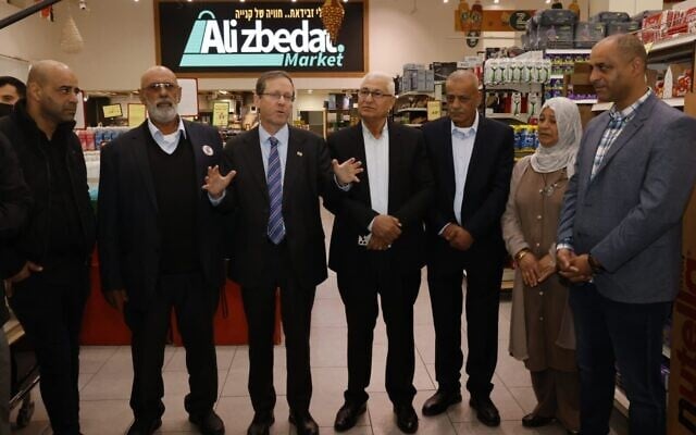 Le président Isaac Herzog (3ᵉ à partir de la gauche) en visite dans l'épicerie d'Ali Zbedat, qui a contribué à déclencher une grève générale dans la société arabe contre la criminalité violente, lors d'un déplacement à Sakhnin en compagnie du maire de cette ville du nord, Mazen Ghnaim (à sa gauche), le 29 janvier 2026. (Crédit : Autorisation) Le président Isaac Herzog (3ᵉ à partir de la gauche) en visite dans l'épicerie d'Ali Zbedat, qui a contribué à déclencher une grève générale dans la société arabe contre la criminalité violente, lors d'un déplacement à Sakhnin en compagnie du maire de cette ville du nord, Mazen Ghnaim (à sa gauche), le 29 janvier 2026. (Crédit : Autorisation)