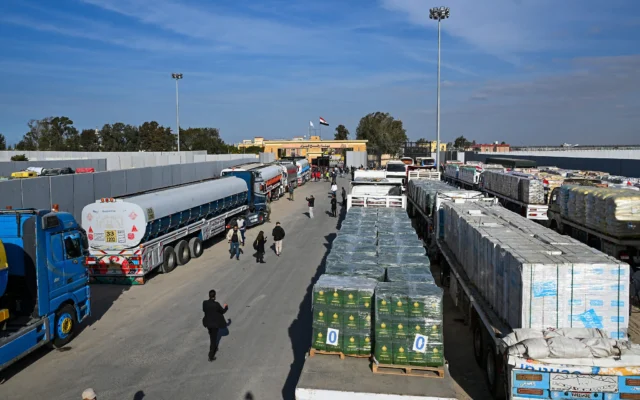 Des personnes passent devant des camions chargés d'aide humanitaire attendant de passer à Gaza depuis le côté égyptien du point de passage de Rafah, le 19 janvier 2025. (Crédit : Khaled Desouki/AFP) Des personnes passent devant des camions chargés d'aide humanitaire attendant de passer à Gaza depuis le côté égyptien du point de passage de Rafah, le 19 janvier 2025. (Crédit : Khaled Desouki/AFP)
