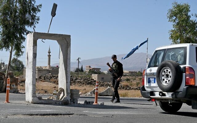 Un véhicule de la Force d'observation du désengagement des Nations unies (FNUOD) passant devant un membre des forces de sécurité syriennes qui monte la garde devant une ancienne base militaire, près de la ville de Quneitra, dans le sud de la Syrie, à la lisière du plateau du Golan, le 21 septembre 2025. (Crédit : Louai Beshara/AFP) Un véhicule de la Force d'observation du désengagement des Nations unies (FNUOD) passant devant un membre des forces de sécurité syriennes qui monte la garde devant une ancienne base militaire, près de la ville de Quneitra, dans le sud de la Syrie, à la lisière du plateau du Golan, le 21 septembre 2025. (Crédit : Louai Beshara/AFP)
