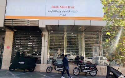 Une Iranienne passe devant une succursale de la banque publique Melli, qui a absorbé les actifs de la défunte banque Ayandeh. Une pancarte en farsi sur la façade indique "Cette ancienne succursale de la banque Ayandeh fait désormais partie de la banque Melli", dans la capitale Téhéran, le 25 octobre 2025. (Crédit : ATTA KENARE / AFP)