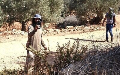 Illustration : Un résident d'implantation utilisant son téléphone pour filmer des Palestiniens et des volontaires étrangers pendant qu'ils récoltent des olives, dans le village palestinien de Turmusaya, près de Ramallah, en Cisjordanie, le 28 octobre 2025. (Crédit : Zain Jaafar/AFP)